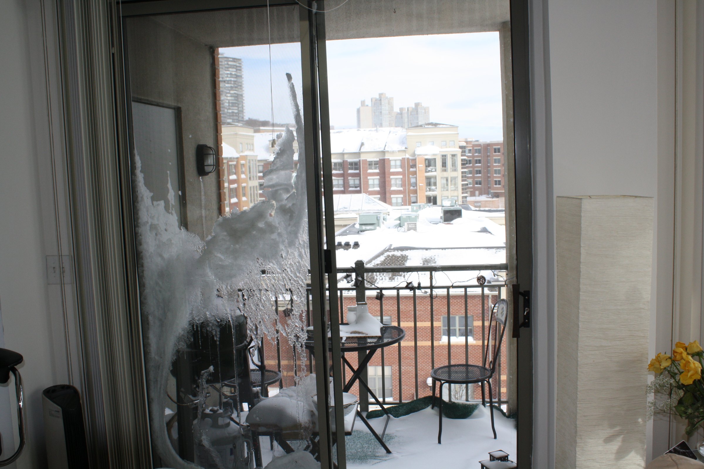 Ice and snow stuck to a sliding glass door beside a snowy balcony.