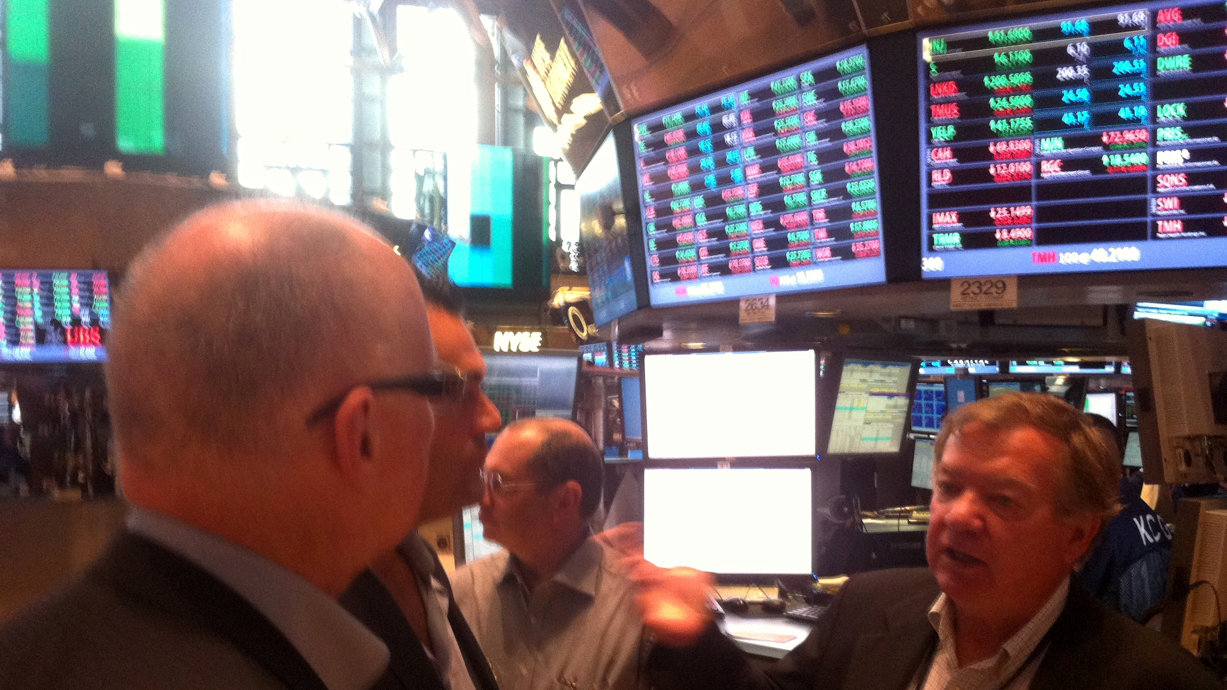 Charlie McLaughlin, at right, explaining the New York Stock Exchange trading floor to members of the Champion Pain Care management team beneath live trading boards.