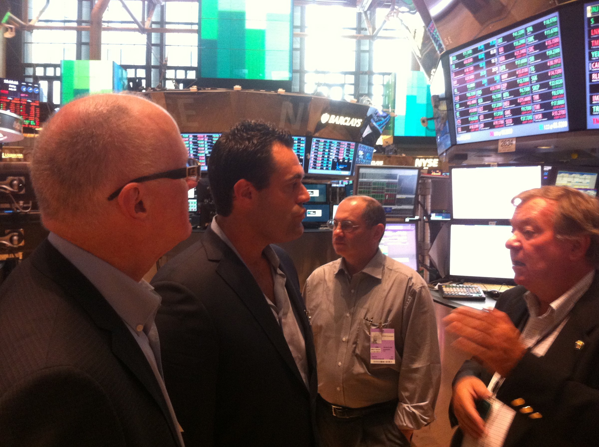 Four men speaking on the New York Stock Exchange floor.