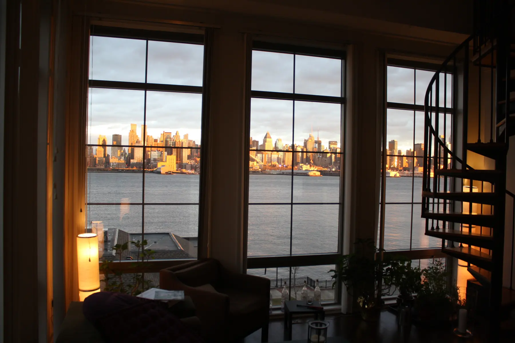 The living room, wall of windows and spiral staircase facing Manhattan.